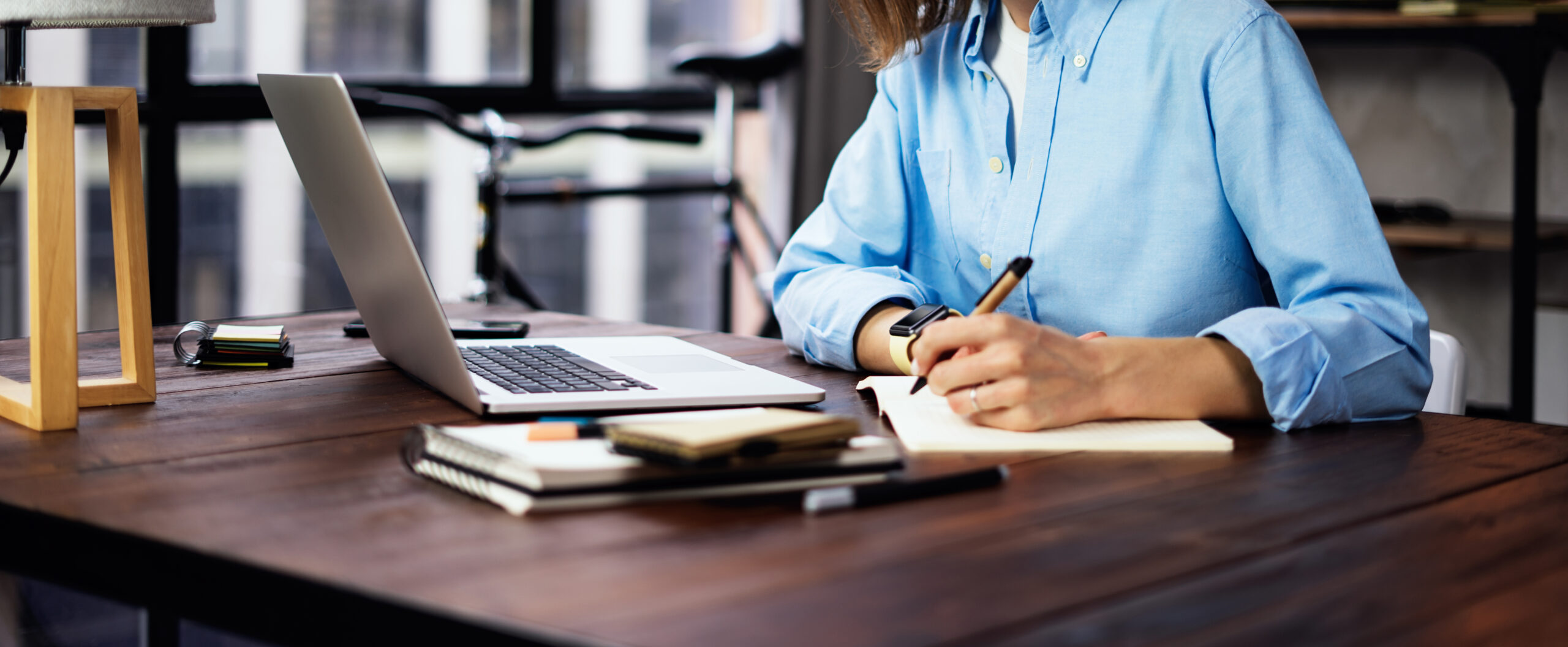 Woman sitting at a desk with a laptop and notepad.